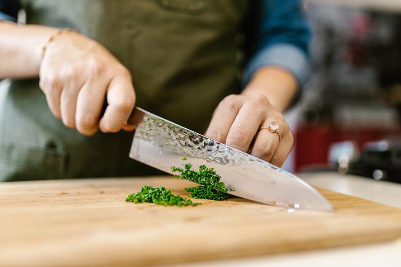 Close-up of a chef slicing fresh herbs on a wooden board in a kitchen.