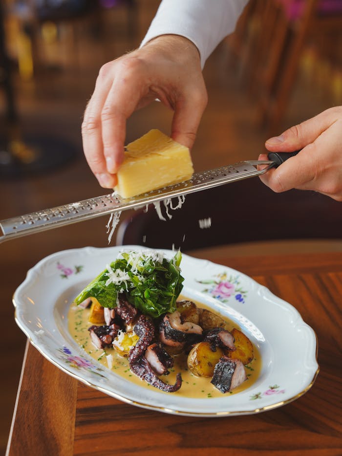 Close-up of cheese being grated over a gourmet meal on a decorative plate.