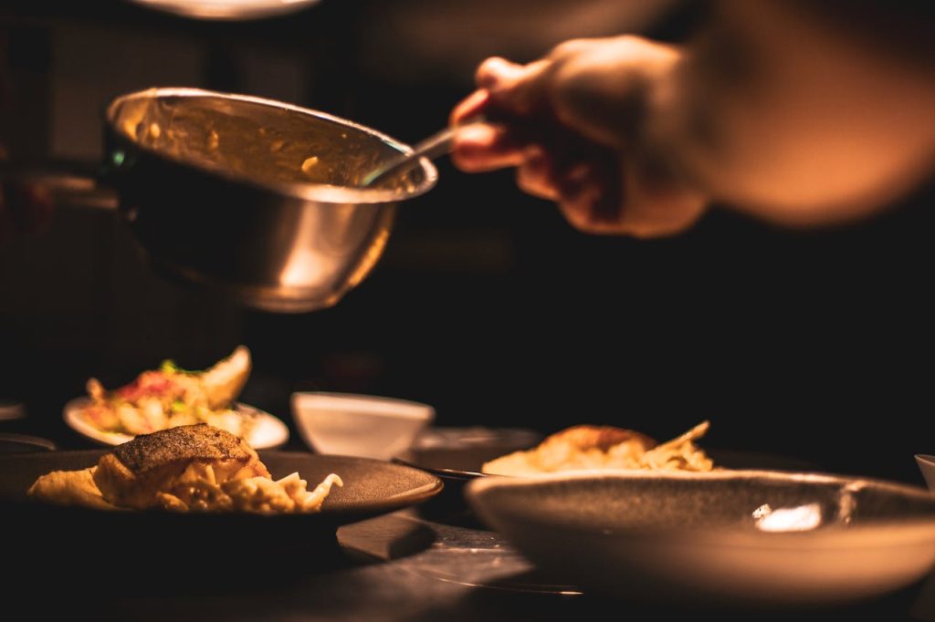 Gourmet dish being plated by a chef in a dimly lit restaurants kitchen.